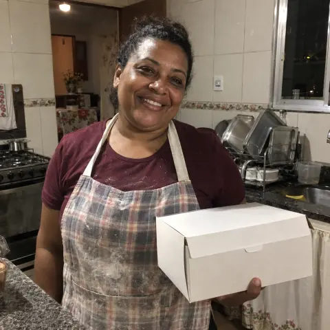 Joana com uma caixa de bolo na cozinha de casa.